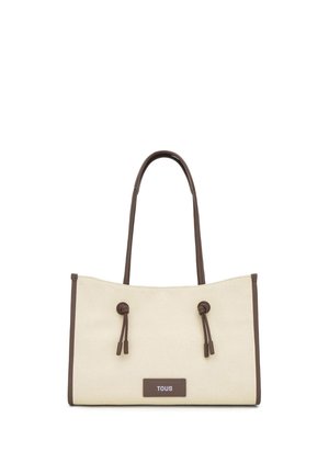 Beżowa torba na ramię z płótna z brązowymi skórzanymi uchwytami, obszyciami i supełkami, z prostokątną metką "TOUS" z przodu.