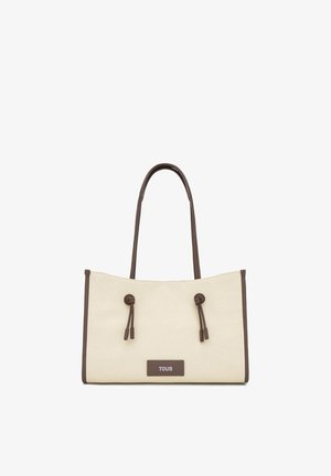 Beige canvas tote bag with brown leather handles, trim, and knots, featuring a rectangular label with "TOUS" on the front.