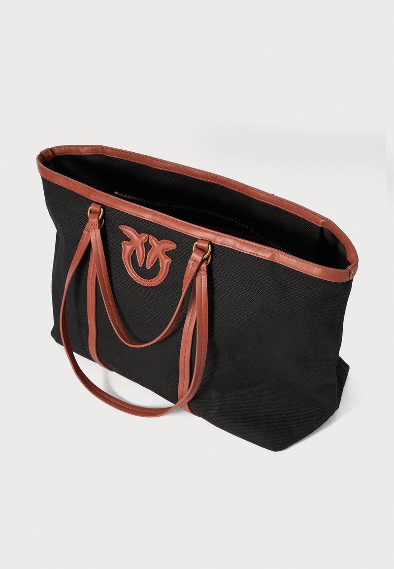 Bolsa de lona negra con asas de cuero marrón. Presenta un logo bordado en la parte frontal y un interior espacioso. Diseño duradero.