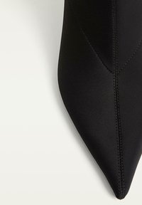 Černá lodička s špičatou špičkou vyrobená z hladkého materiálu s dekorativním šitím podél švů. Elegantní design s matným povrchem.