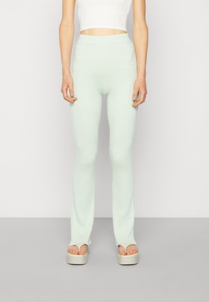 Leggings de malha canelada, em verde menta, com cintura alta, apresentando um design ajustado e bainhas ligeiramente largas, combinadas com sandálias de plataforma.