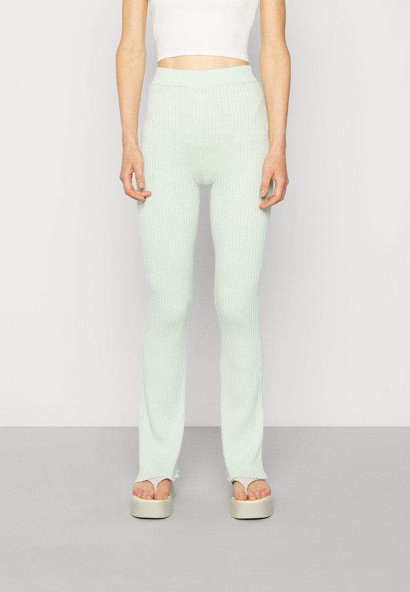 Leggings de malha canelada, em verde menta, com cintura alta, apresentando um design ajustado e bainhas ligeiramente largas, combinadas com sandálias de plataforma.