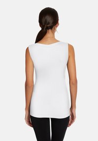Top bianco senza maniche con scollatura rotonda, design aderente e texture liscia; abbinato a leggings neri, visto da dietro.