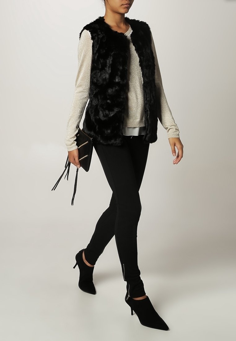 Musta tekoturkisliivi kimaltavan beigen neuleen päällä, yhdistetty mustiin legginsseihin ja teräväkärkisiin korkokenkiin. Asusteina pieni musta clutch-laukku.