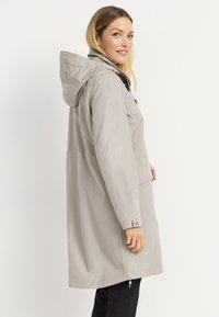 Lichtgrijze, hooded regenjas met een losse pasvorm, ritssluiting aan de voorkant en zijzakken. Heeft knoopmanchetten en een getailleerde taille voor een verstelbare vorm.