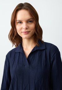 Maglione lavorato a maglia blu navy con colletto, motivo geometrico testurizzato e maniche ad altezza intermedia. Materiale morbido con vestibilità rilassata.