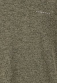 Oliivinvihreä urheilupaita, joka on valmistettu teksturoidusta kankaasta. Paidan vasemmassa yläkulmassa on valkoisella tekstillä sana "KESTÄVYYS".