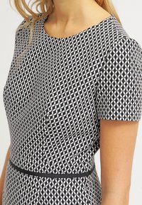 Robe à manches courtes avec un motif géométrique noir et blanc. Présente un col rond et une ceinture noire contrastante.