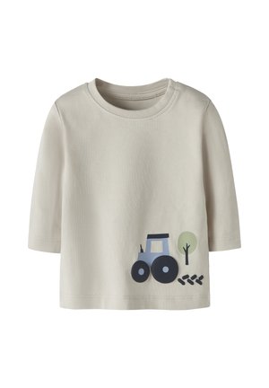 Camiseta beige de manga larga para niño pequeño con un pequeño tractor azul, un árbol verde y un dibujo de huellas de neumáticos negras cerca del dobladillo inferior en la parte delantera.