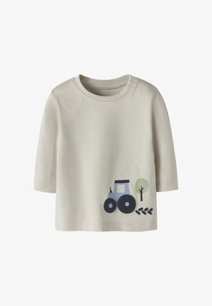 Camiseta beige de manga larga para niño pequeño con un pequeño tractor azul, un árbol verde y un dibujo de huellas de neumáticos negras cerca del dobladillo inferior en la parte delantera.