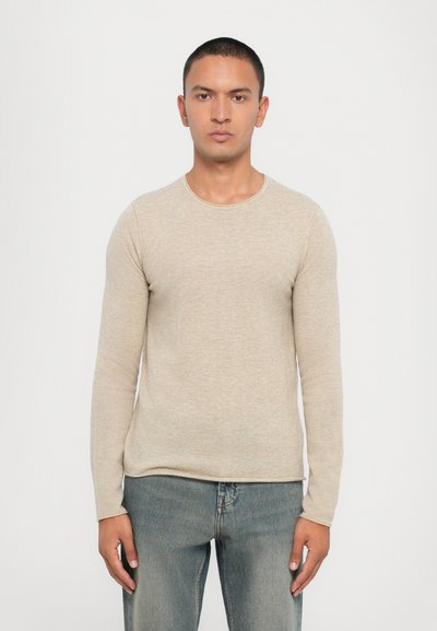 Beige long-sleeve shirt with a round neckline, made of soft fabric. The design features a slim fit and smooth texture, paired with denim jeans.