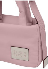 Růžová polstrovaná kabelka s hladkým povrchem, zdobená prošívanými detaily a bílým obdélníkovým štítkem s nápisem "STUDIO BERLIN."
