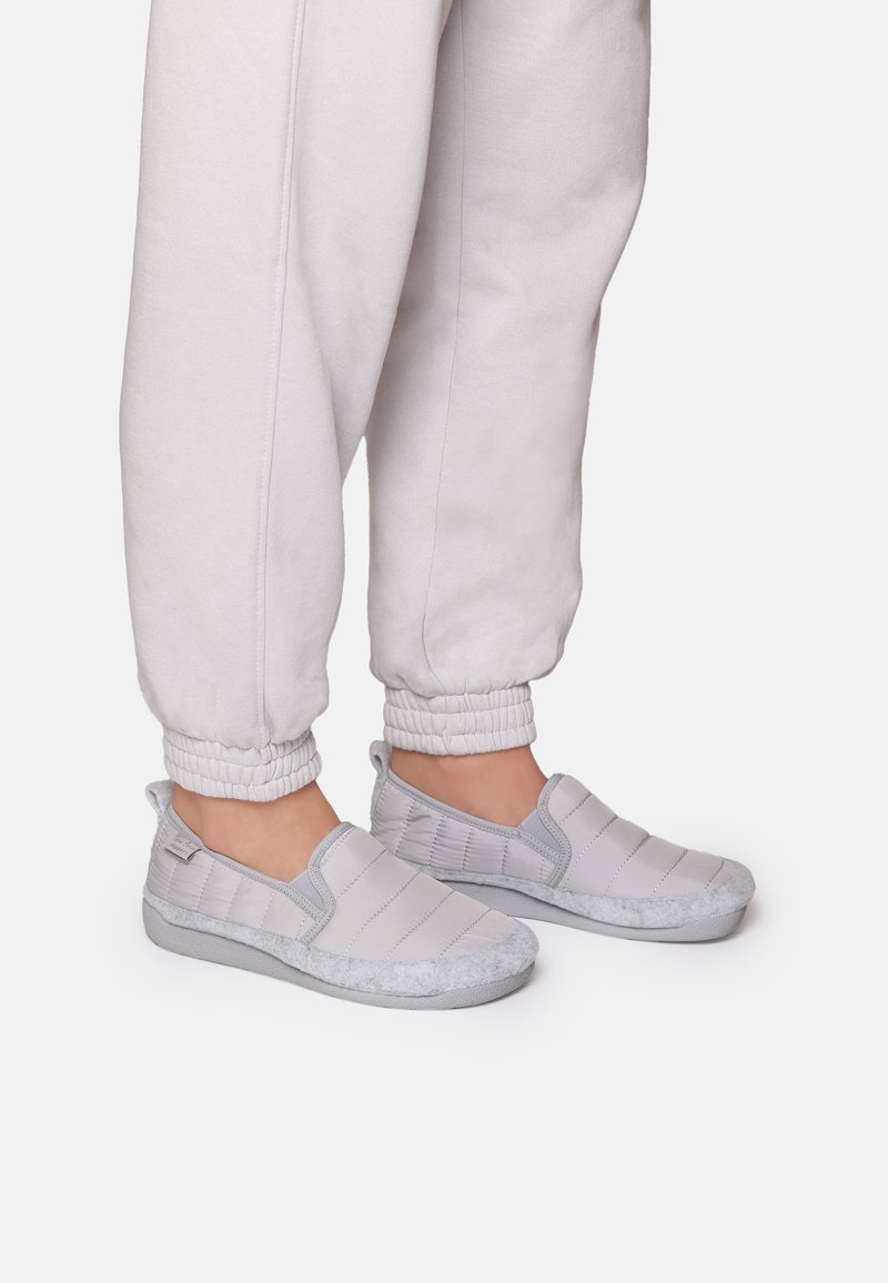 Sive slip-on cipele imaju kviltani dizajn s dlakavim, sivo krznom i teksturiranim sivim potplatom, u kombinaciji s svijetlosivim jogger hlačama.