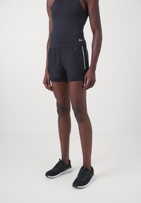Mustat urheilushortsit, joissa on valkoiset sivuraitat, valmistettu kevyestä kankaasta, yhdistettynä tiukkaan mustaan tank top -paitaan ja mustiin juoksukenkiin.
