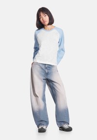 Koszulka raglan z długim rękawem, białym tułowiem i jasnoniebieskimi rękawami, zestawiona z jasnoniebieskimi wyblakłymi jeansami o szerokich nogawkach i czarnymi trampkami.