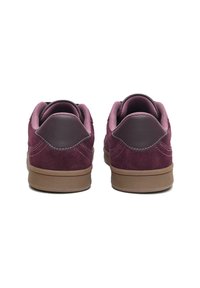 Tenisi din suede într-o nuanță adâncă de burgundy, cu talpă din cauciuc în ton. Vederea din spate arată gulerul căptușit și accentele sintetice contrastante în burgundy.
