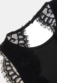 Tessuto nero con dettagli in pizzo presenta motivi floreali e bordi frangiati. Include una chiusura a bottoni sul retro del collo.