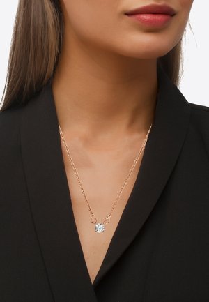 Roze goud ketting met een enkele heldere edelsteen hanger, gedragen tegen een zwarte blouse, die het elegante ontwerp benadrukt.