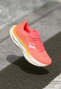 Sapatilha de corrida rosa brilhante com um parte superior em malha leve, sola acolchoada e detalhes em faixa branca. Projetada para desempenho e conforto.