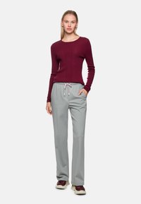 Bordeauxroter, figurbetonter Pullover mit Rippenstruktur und rundem Ausschnitt, kombiniert mit hellgrauen, gestreiften, schmal zulaufenden Hosen mit Kordelzugbund.