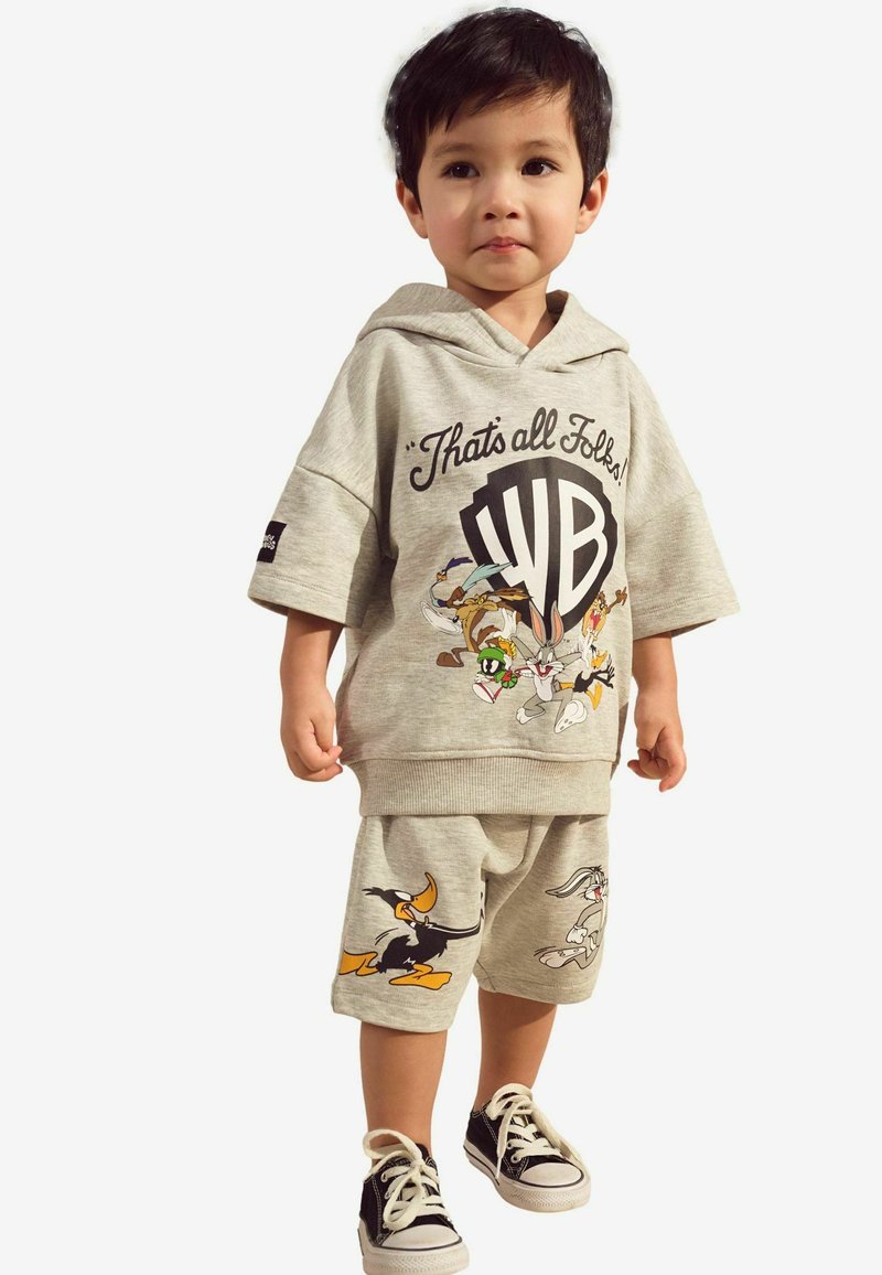 Ljusgrå huvtröja med tecknad grafik och slogan, tillsammans med matchande shorts prydda med figurer. Svarta sneakers fulländar outfiten.
