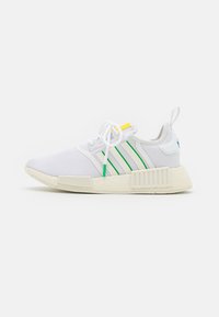 Zapatillas deportivas blancas con parte superior de malla, acentos en verde y amarillo, y tres rayas blancas. Suela de goma gruesa y texturizada con marca.