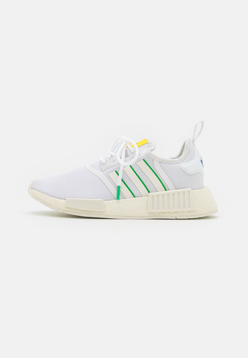 Zapatillas deportivas blancas con parte superior de malla, acentos en verde y amarillo, y tres rayas blancas. Suela de goma gruesa y texturizada con marca.