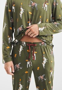 Oliveově zelená pyžamo s hravými ilustracemi psů držících fotbaly, s dlouhými rukávy, elastickým pasem a stahovací šňůrkou.