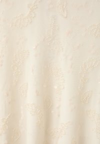 Tissu transparent couleur crème avec des motifs floraux subtils composés de petites perles et sequins dispersés sur toute la surface.