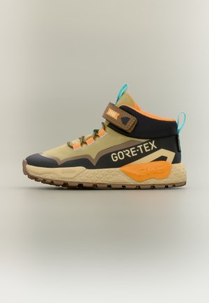 Chaussure de randonnée Gore-Tex montante beige, noire et orange avec sangle marron, languettes bleues et semelle texturée pour une utilisation en extérieur.