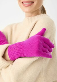 Fuchsia gebreide handschoenen met geribde manchetten, voorzien van een bloemembroidery detail. Ggedragen over een crèmekleurige trui. Glad textuur.