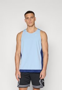 Lyseblå sportstopp med meshstruktur, marineblå sidestykker og rund halslinning. Kombinert med svarte shorts. Nike-logo på brystet.