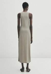 Robe débardeur longue et ajustée en tissu beige clair au toucher lisse, présentant une silhouette droite et des fentes sur les côtés pour plus de liberté de mouvement.