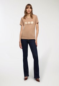 Beżowa koszulka z krótkim rękawem z nadrukiem ust i napisem "melt in love", w połączeniu z ciemnoniebieskimi spodniami w stylu dzwonów i brązowymi spiczastymi butami.