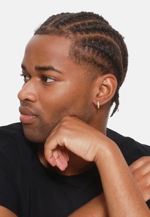 Gold hoop earring, textured design, worn on a person with braided hair. Black t-shirt, light skin tone, hand resting on chin.