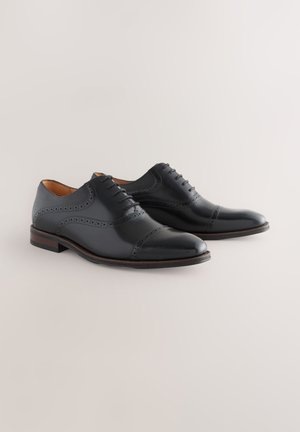 Schwarze Lederschuhe mit polierter Oberfläche, Brogue-Details und rundem Zehenbereich. Sie verfügen über ein schnürbares Design und eine Holzsohle.
