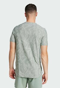 Ljusgrön atletisk t-shirt med ett texturerat zigzag-mönster och korta ärmar. Den har en rundad halsringning och en något förlängd bakre fåll.