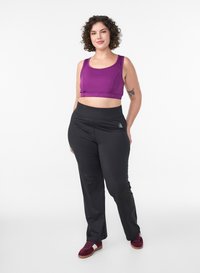 Lila Sport-Crop-Top und schwarze, hoch taillierte Sporthose. Das Outfit zeichnet sich durch eine glatte Textur und ein eng anliegendes Design aus, mit einem Logodetail auf der Hose.