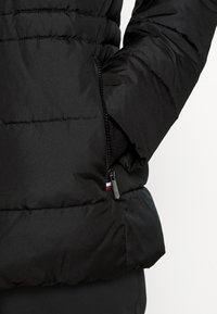 Black puffer jacket featuring a zippered side pocket, quilted texture, and contrasting colored accent near the zipper. Soft, insulated material.