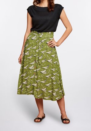 Jupe verte avec un motif de bateau à voile, dotée d'une taille nouée, d'accents de boutons et d'un design fluide. Associée à un haut noir à manches courtes.