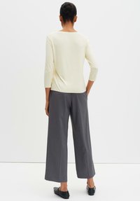 Beige driekwart mouw top met een ronde hals, gecombineerd met hoge taille grijze wijde broek en zwarte instapschoenen.