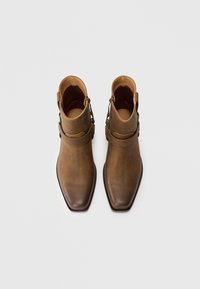 Botas de tobillo de cuero marrón con puntera afilada, tira en el tobillo y herrajes metálicos, con un acabado suave y un diseño minimalista.