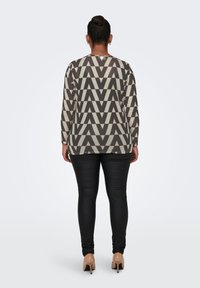 Maglia a maniche lunghe color crema e grigio con un audace motivo geometrico, abbinata a leggings neri e tacchi nudi. Tessuto dalla superficie liscia.
