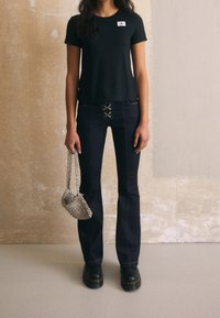 T-shirt nera a maniche corte con patch logo, jeans a zampa d'elefante blu scuro con lacci sul davanti, borsa a catena argento e scarpe platform nere.