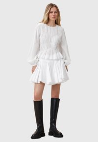 Wit peplum top met gerimpelde textuur en lange mouwen, gecombineerd met een flared witte minirok. Zwarte kniehoge laarzen maken de look compleet.