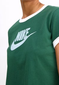 Grön bomullströja med vit ribbad krage, med en stor vit Nike-logotyp på framsidan. Korta ärmar med kontrasterande trim.