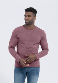 Langarm-Crewneck-Shirt in sanftem Mauve, aus weichem Baumwollmaterial, mit gerippten Details am Kragen und einer figurnahen Silhouette.