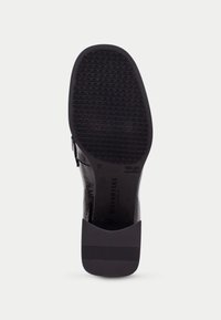 Suela de zapato negra con un patrón de agarre texturizado, un tacón liso con forma curva y un diseño de plataforma robusta y ligeramente elevada.