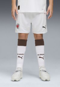Vita fotbollsshorts med svart Puma-logga, brunt accentuerade knästrumpor med texten "ST. PAULI", och fotbollsskor med grå snören.