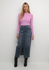 Top à manches longues en maille côtelée rose clair associé à une jupe maxi en jean taille haute avec une fente devant et des bottines noires.